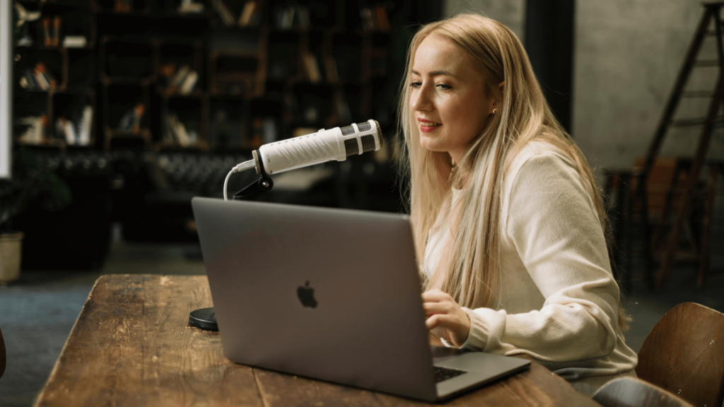 Jessica sitzt an einem Tisch und spricht ins Mikrofon, denn sie nimmt eine Podcastfolge auf
