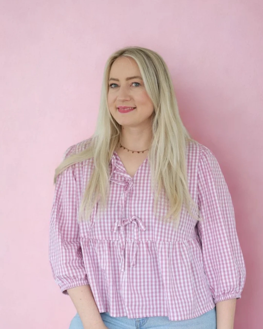 Portrait von Jessica in karierter Bluse vor einer rosa Wand